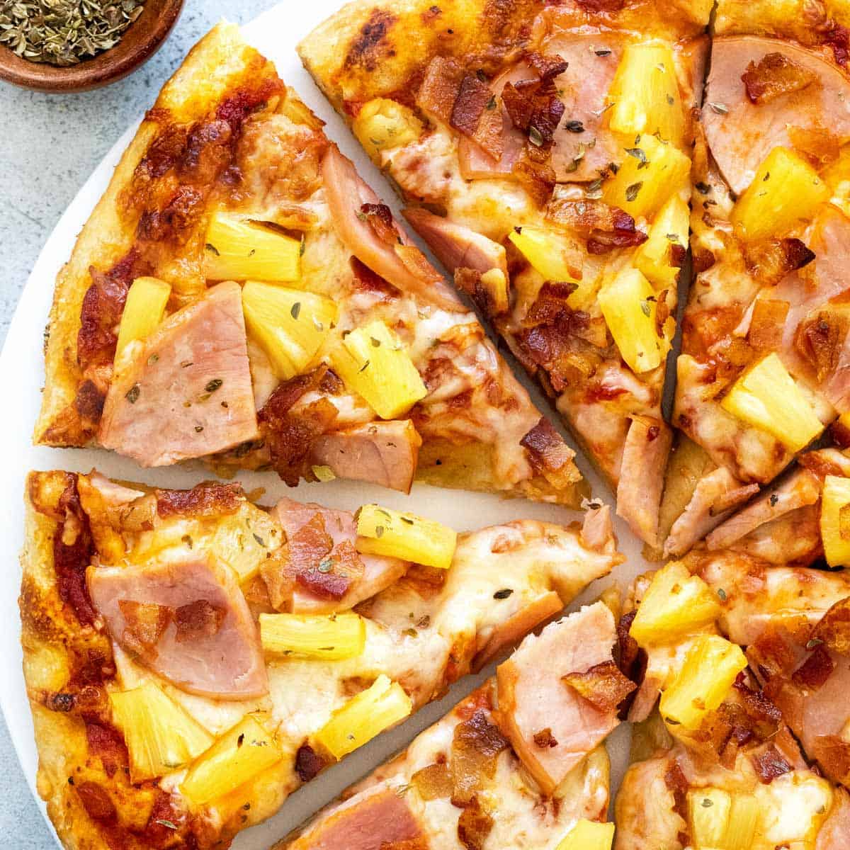 A cheesy and delicious looking slice of canadian pizza with herbs and spices all over.