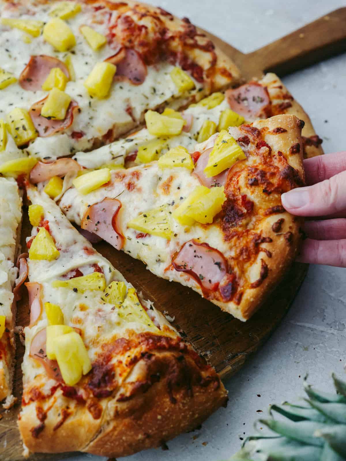 A mouth watering cut pineapple pizza with crumbled bacon, sweet pineapple chunks and delicious looking ham as toppings with undoubtedly flavourful herbs to boot.
